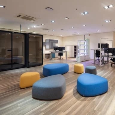Großraumbüro mit Büroeinrichtung von lento, in der Mitte eine Ruhezone mit Sitzhockern, im Hintergrund mehrere Einzelarbeitsplätze mit höhenverstellbaren Steh-Sitz-Schreibtischen und Bürostühlen