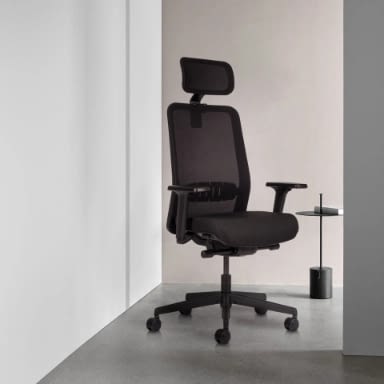 In Seitenansicht ist der ergonomische Bürostuhl lento proto in Schwarz mit Kopfstütze neben einem Tisch vor neutralem Hintergrund im Homeoffice platziert.