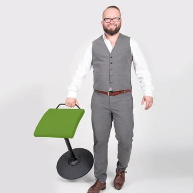 Im Arbeitskontext ist der Stehhocker sella activa in grün von lento mit einer Person beim Tragen dargestellt.