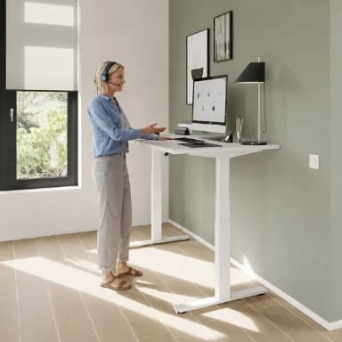 Höhenverstellbarer Schreibtisch elektrisch in weiß im Homeoffice, Person arbeitet im Stehen mit Headset am PC an einem Steh-Sitz-Schreibtisch in heller Wohnbüroumgebung, ergonomischer Arbeitsplatz made in Germany, lento