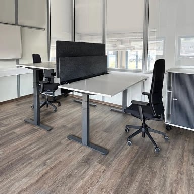 Höhenverstellbarer Schreibtisch elektrisch mit Doppelarbeitsplatz, Akustik Trennwand und zwei schwarzen Bürostühlen agilis matrix in moderner Büroeinrichtung, Stehschreibtisch für ergonomische Arbeitsplätze, Hersteller lento