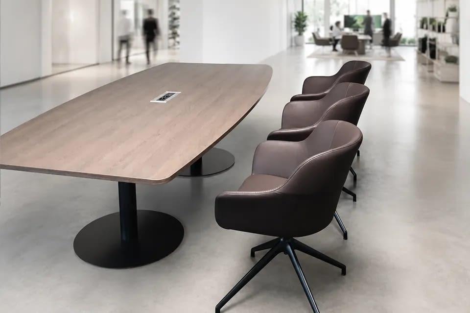 Im hellen Büro stehen ergonomische Konferenz- und Drehstühle mit Armlehnen an einem Konferenztisch mit dunkler Holzplatte, ergänzt durch drei Schalenstühle aus Echtleder in Marron.