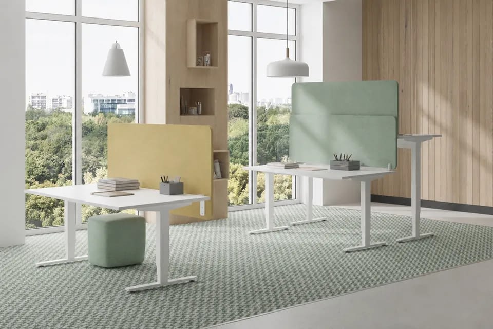 Höhenverstellbare elektrische Schreibtische in Weiß in einem hellen Büro hintereinander angeordnet, jeweils mit am Tisch montierter Akustiktrennwand in Mintgrün und Gelb.
