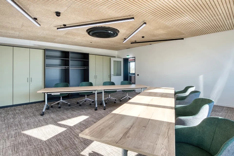 Ergonomische grüne Drehstühle mit Armlehnen in einem großen Büro, für ein Meeting arrangiert, kombiniert mit rollbaren Schreibtischen mit Holzplatten.