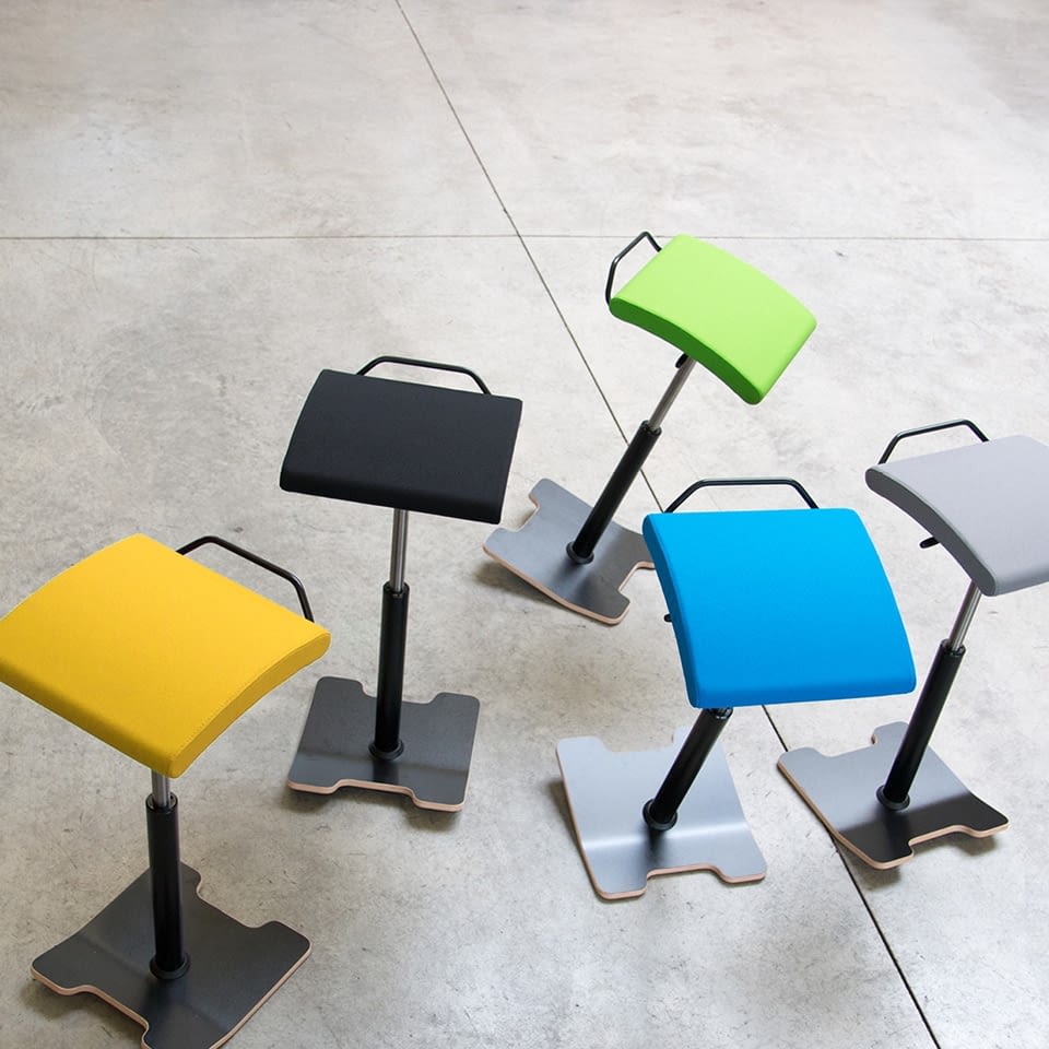 In der Draufsicht sind Stehhocker sella activa mit Bodenwippe in blau, gelb, schwarz, grau und grün in der Produktionshalle von lento angeordnet.