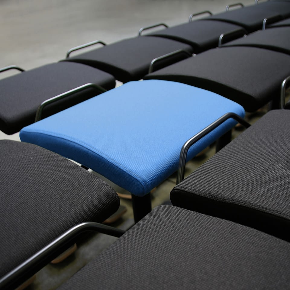 Aus einem schrägen Blickwinkel ist eine blaue Sitz Stehhilfe vor mehreren schwarzen Sitz Stehhilfen positioniert.
