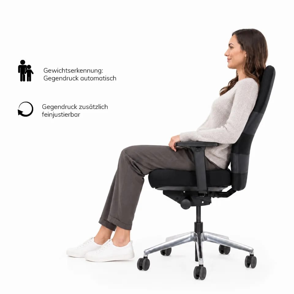 Eine Person lehnt sich auf dem agilis comfort Bürostuhl in schwarz zurück, während die Sitzposition die automatische Gewichtserkennung sichtbar aktiviert.