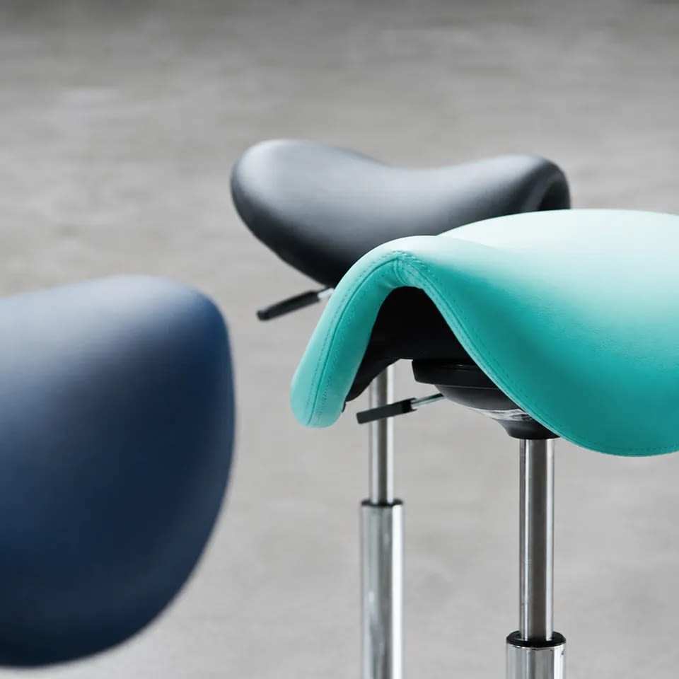 Der ergonomische sella Sattelhocker ist in Blau, Schwarz und Dunkelblau in einer Nahaufnahme dargestellt, sodass seine Form gut erkennbar ist.