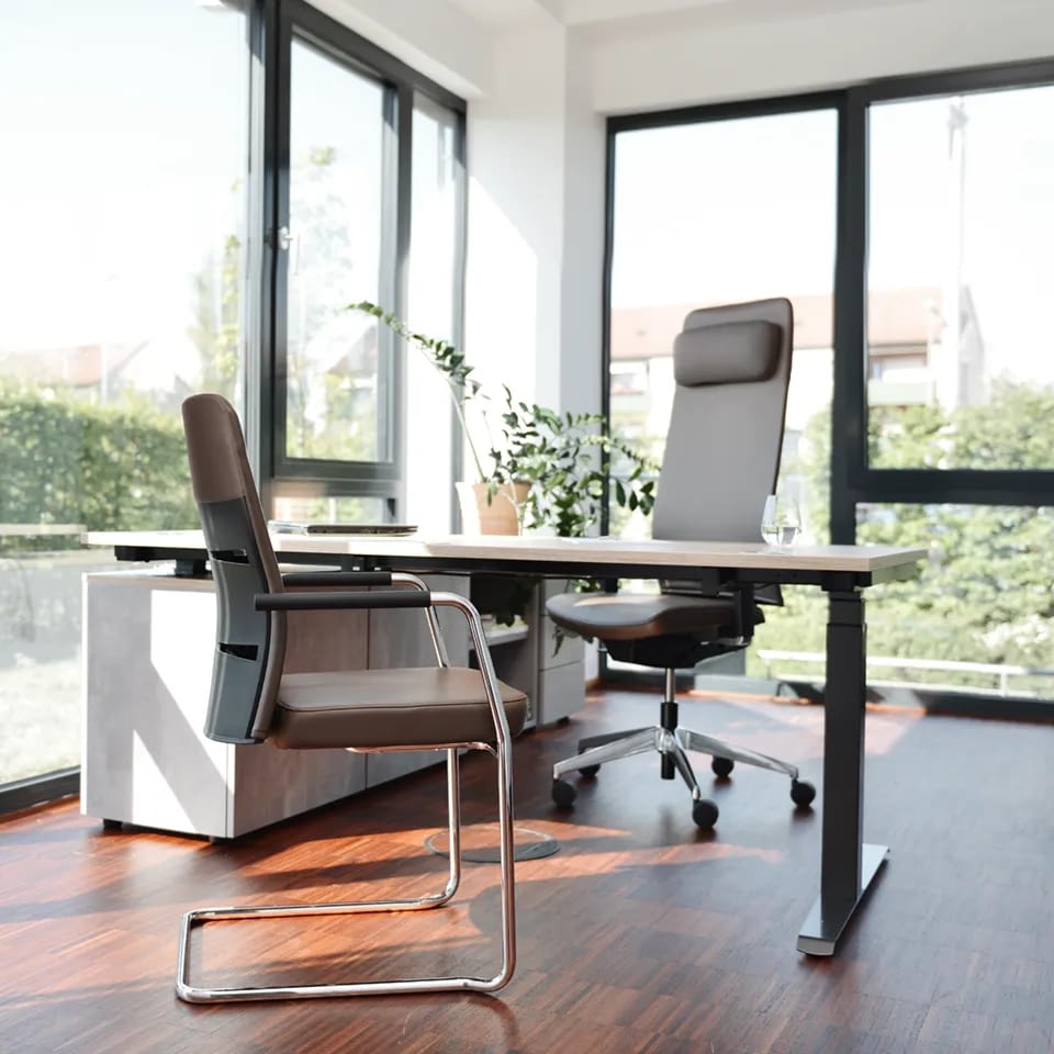 Im Büroarrangement ergänzt ein Chefsessel agilis matrix in echtem Leder braun zusammen mit einem höhenverstellbaren Steh-Sitzschreibtisch und einem Besucherstuhl aus echtem Leder braun die Einrichtung.