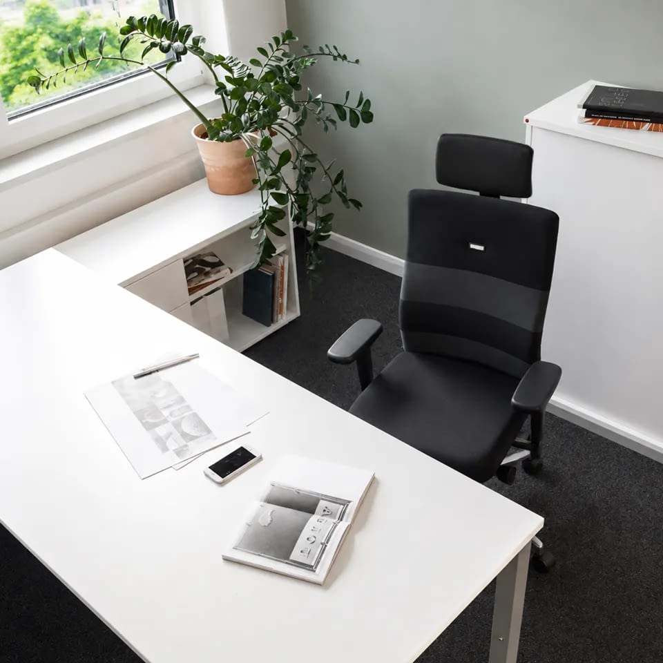 Aufsicht des ergonomischen Bürostuhls agilis comfort in Schwarz-Grau mit Kopfstütze neben einem Schreibtisch.