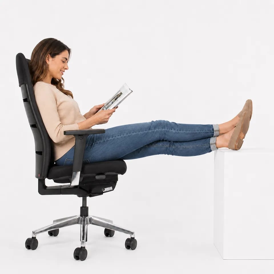 Seitlich sitzt eine Person mit hochgelegten Beinen im ergonomischen Bürostuhl agilis matrix comfort in schwarz mit Netzrücken.