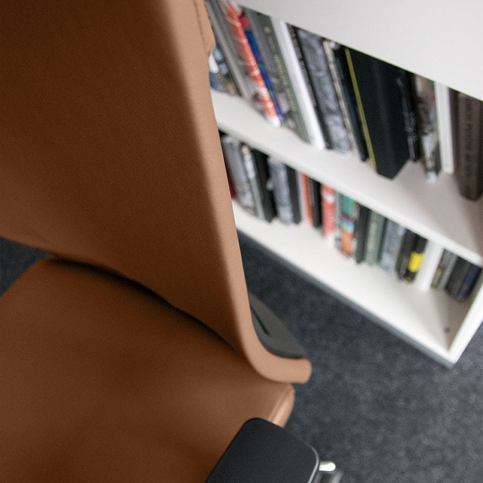 In Draufsicht ist die Rückenlehne des ergonomischen Bürostuhls agilis matrix comfort in Echtleder calvados dargestellt, im Hintergrund befindet sich ein Regal mit Büchern.