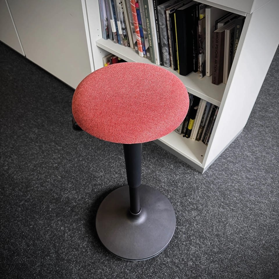 Der Stehhocker sella flex in korallenrot ist in der Detailaufnahme zu sehen, Sitzfläche und Materialstruktur sind sichtbar.
