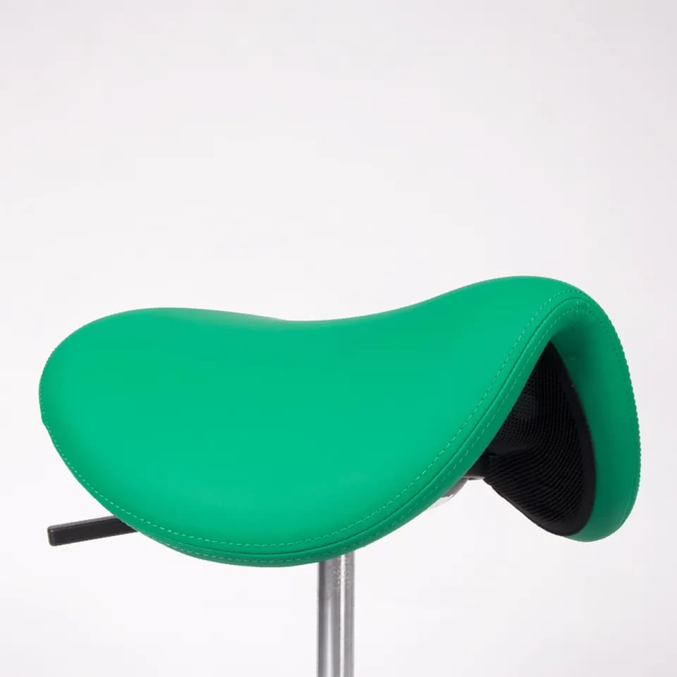 In der Nahaufnahme zeigt sich der ergonomische Sattelhocker sella in Grün mit Sattelsitz, dessen Lederstruktur und feine Oberflächenverarbeitung deutlich erkennbar sind.