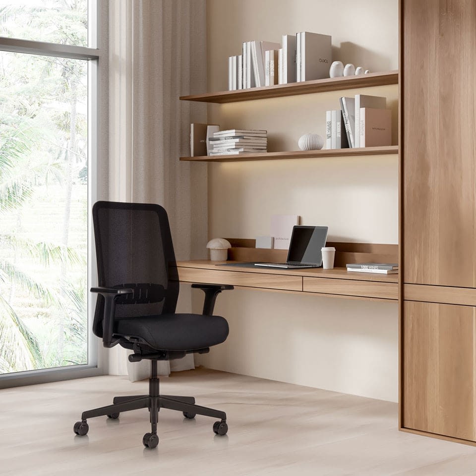 In einer Homeoffice-Umgebung steht der ergonomische Bürostuhl proto in Schwarz mit Netzrücken leicht schräg an einem Schreibtisch.